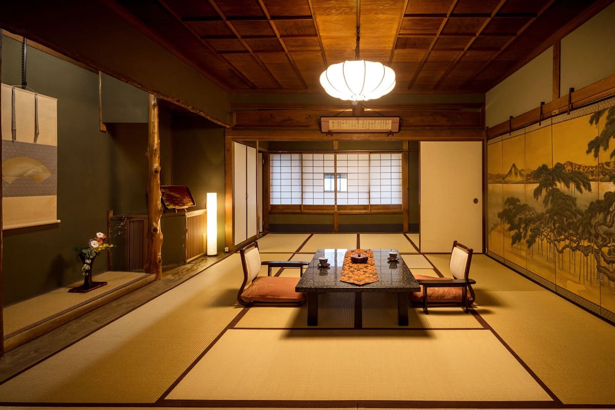 A traditional Japanese room with tatami flooring, a low table with cushions, a shoji screen, and a hanging scroll.