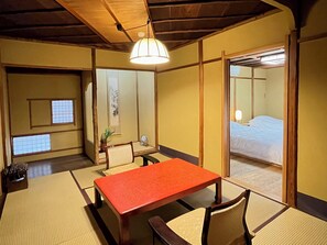 A traditional Japanese room with tatami flooring, a low wooden table, and a bed with a white mattress.
