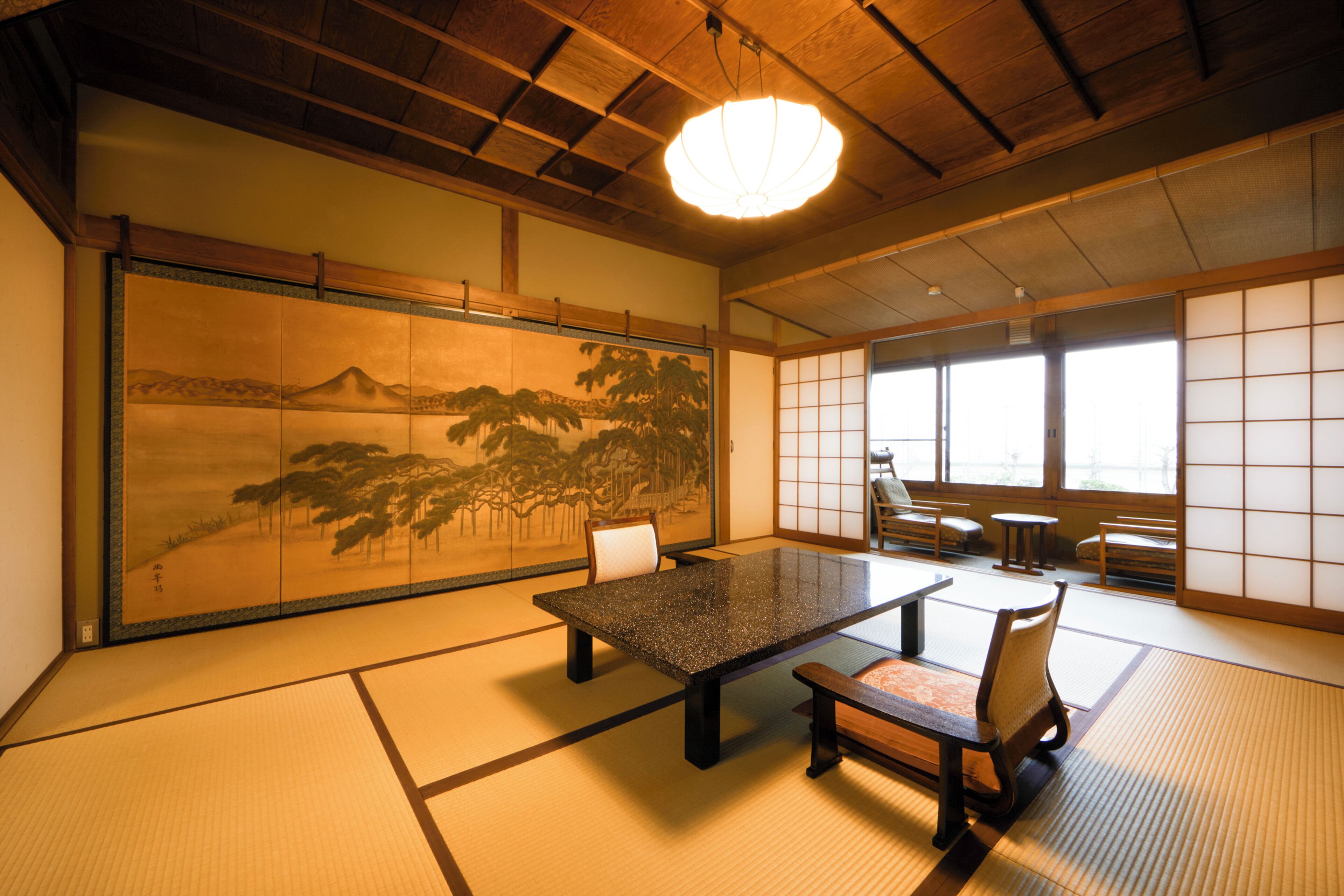 A traditional Japanese room with tatami flooring, a low table, and a large shoji screen depicting a landscape.