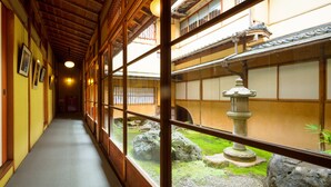 Un pasillo japonés tradicional con suelo de tatami, puertas correderas y vistas a un jardín con un farol de piedra.