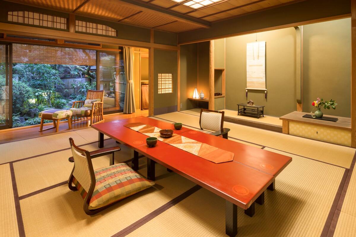 Um quarto tradicional japonês, com tatames, uma mesa baixa e portas deslizantes para um jardim.