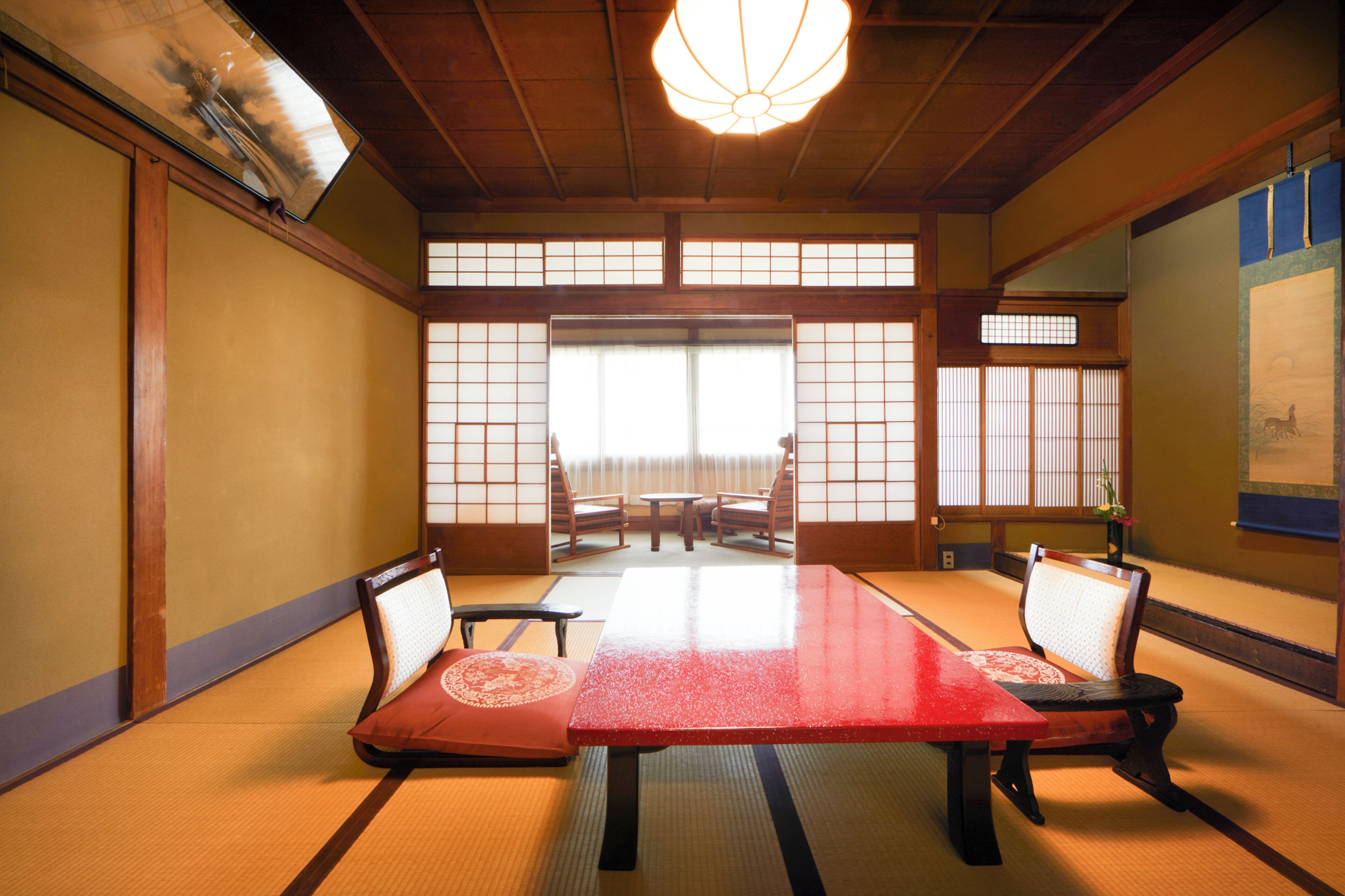 Una habitación japonesa tradicional con tatamis, una mesa baja, cuatro esterillas de tatami, dos sillas y puertas correderas.