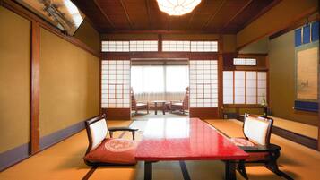 Una habitación japonesa tradicional con tatamis, una mesa baja, cuatro esterillas de tatami, dos sillas y puertas correderas.