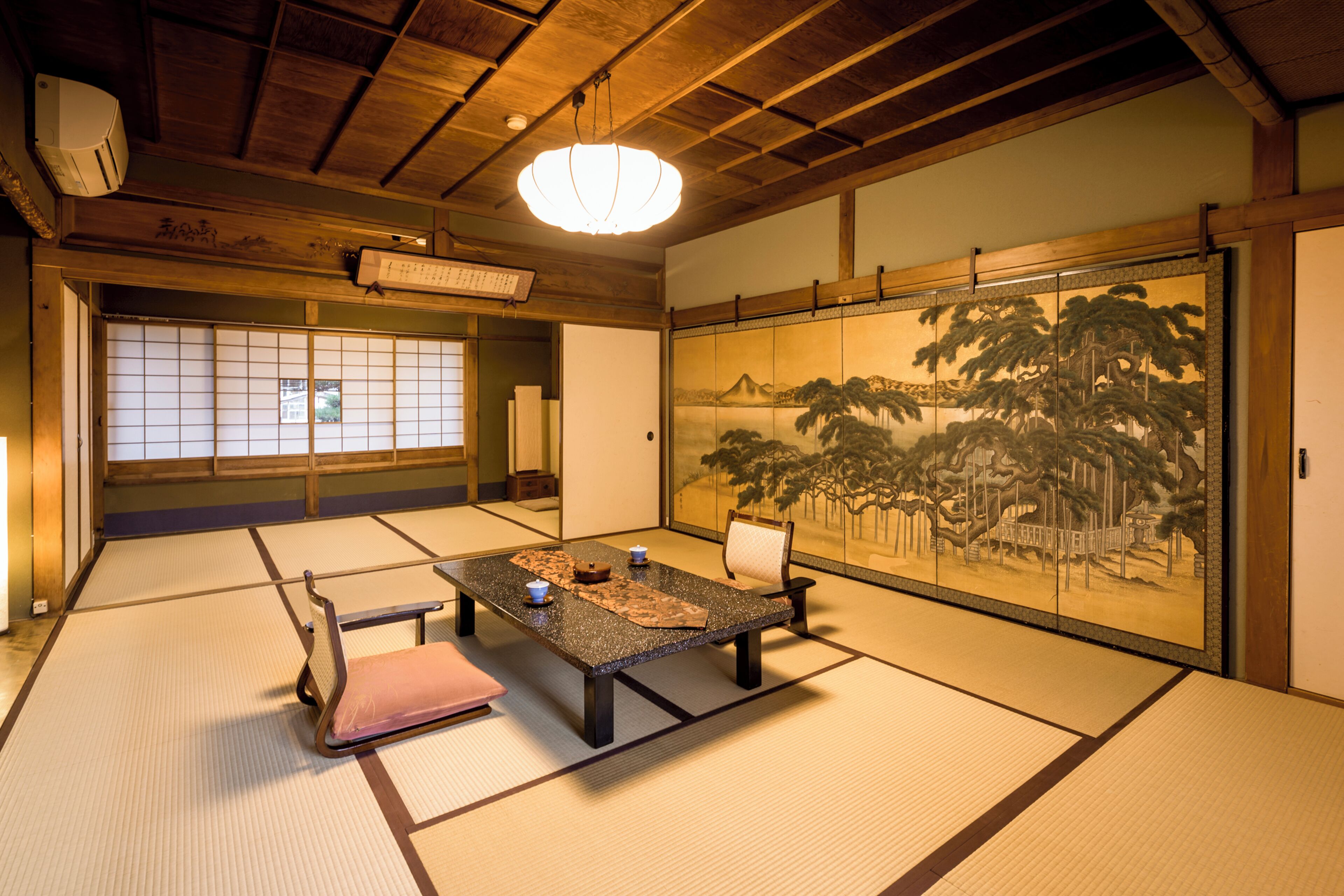Una habitación japonesa tradicional con suelo de tatami, una mesa baja con cojines y un puertas correderas decoradas con una pintura de paisaje.