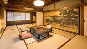 Una habitación japonesa tradicional con suelo de tatami, una mesa baja con cojines y un puertas correderas decoradas con una pintura de paisaje.