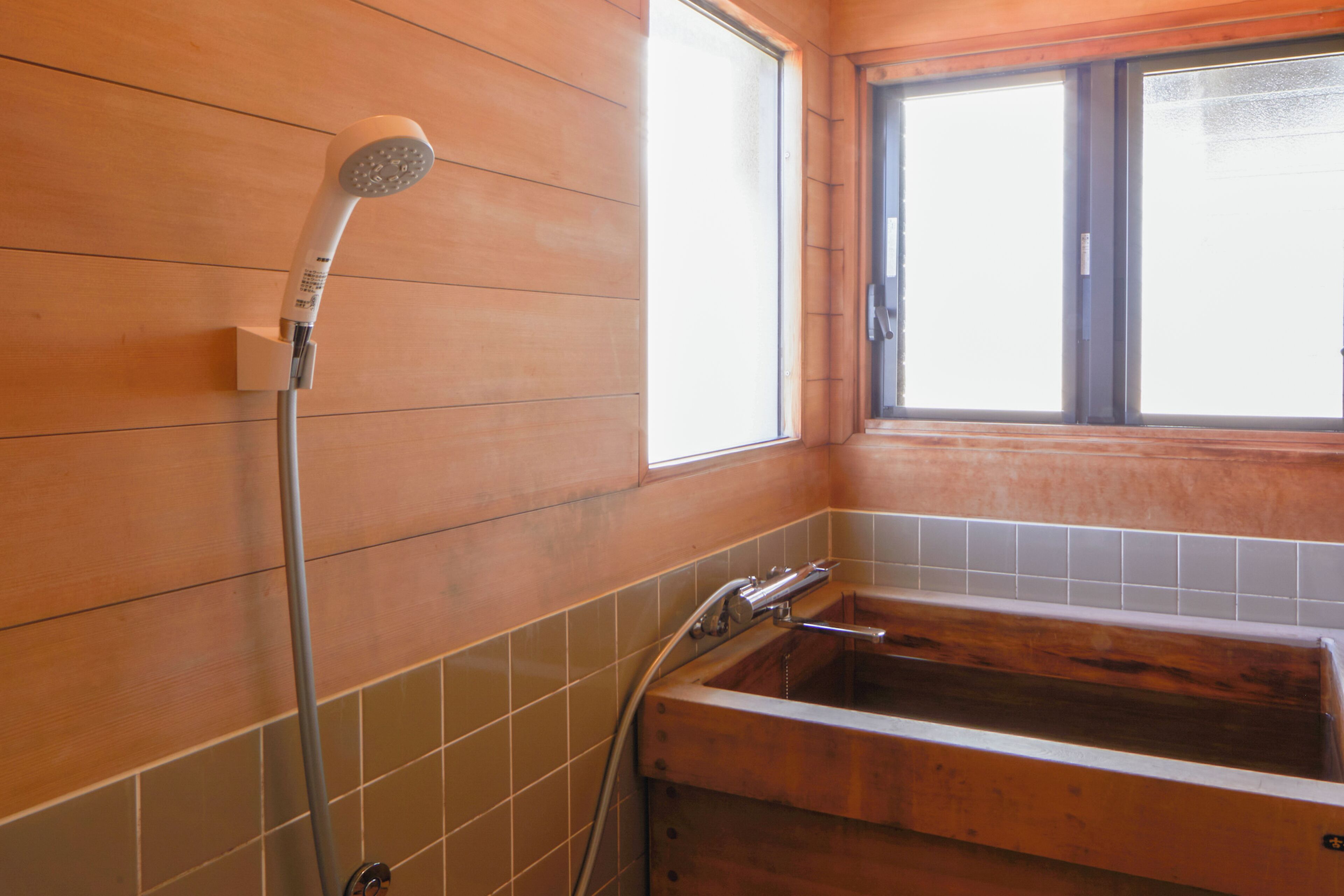 Un baño con una bañera de madera, un cabezal de ducha y una ventana.