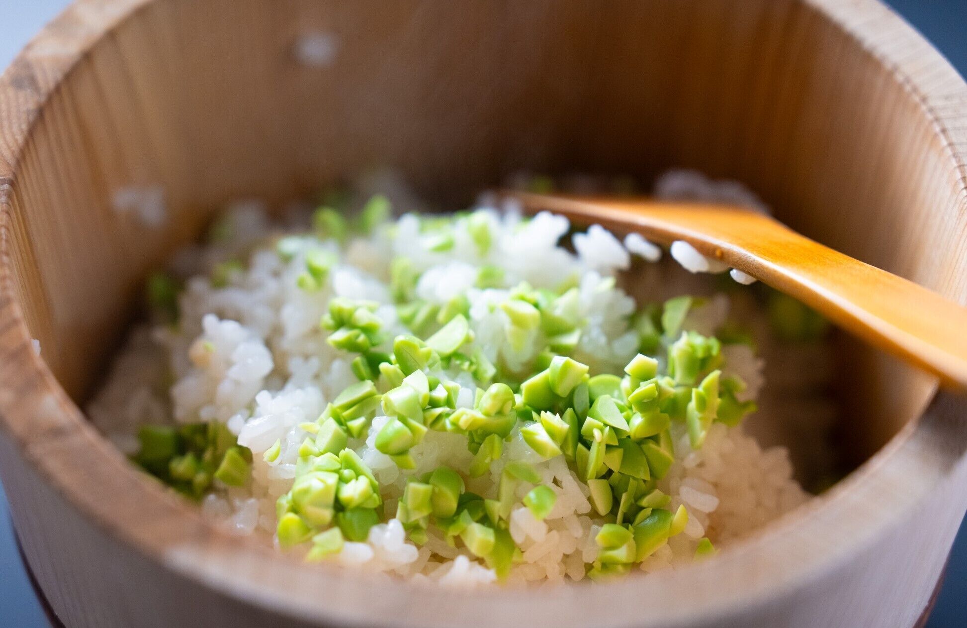 A wooden bowl containing rice and chopped green vegetables.