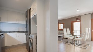 A modern kitchen with a washing machine, a glass dining table with chairs, and a living area with a sofa and a coffee table. - MEDITERRANEAN APARTMENT 3 minutes TO THE BEACH 2 (Tossa de Mar)