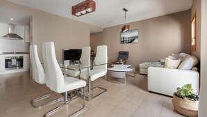 A modern living room with a glass dining table, white chairs, a white sofa, a coffee table, and a painting on the wall. - MEDITERRANEAN APARTMENT 3 minutes TO THE BEACH 2 (Tossa de Mar)