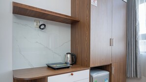 A compact kitchenette with a marble backsplash, wooden cabinetry, a small refrigerator, and a countertop with a kettle and a book. - S HOTEL BEACH DA NANG (Da Nang)