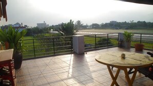Een balkon met een betegelde vloer, een ronde houten tafel en planten in potten.