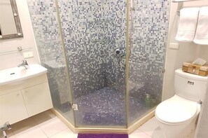Een badkamer met een douchecabine van glas, een wit wastafelmeubel en een toilet.