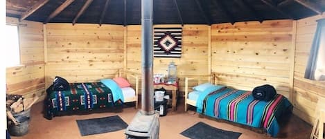 A cozy cabin with two wooden beds, a central table, and a decorative wall hanging.