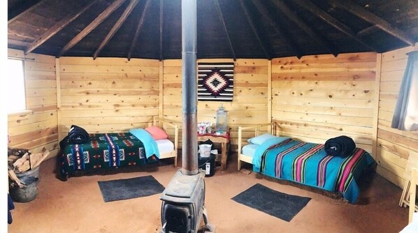 A cozy cabin with two wooden beds, a central table, and a decorative wall hanging.