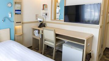 A hotel room with a bed, a desk with a chair, a small refrigerator, a television, a mirror, a clock, and a thermostat.