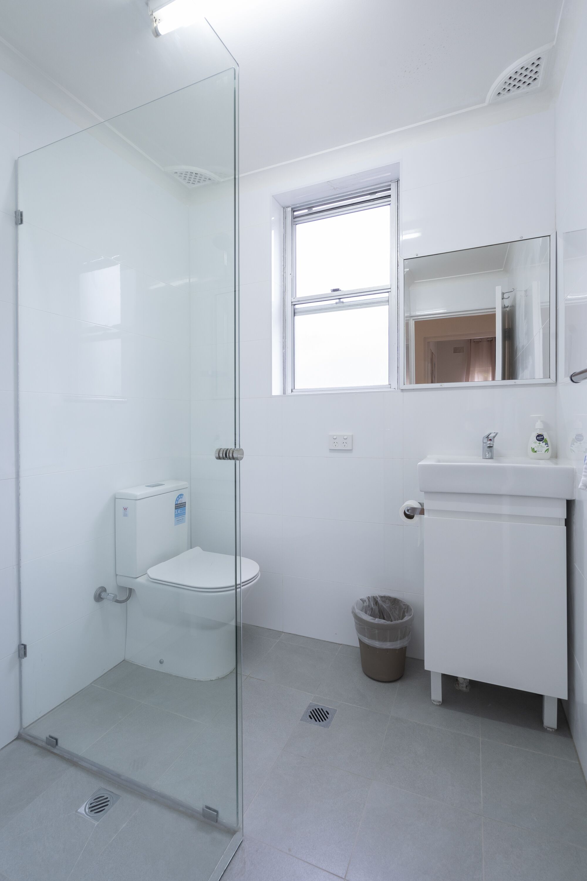 A modern bathroom with a glass-enclosed shower, a toilet, a sink, and a window above the sink.