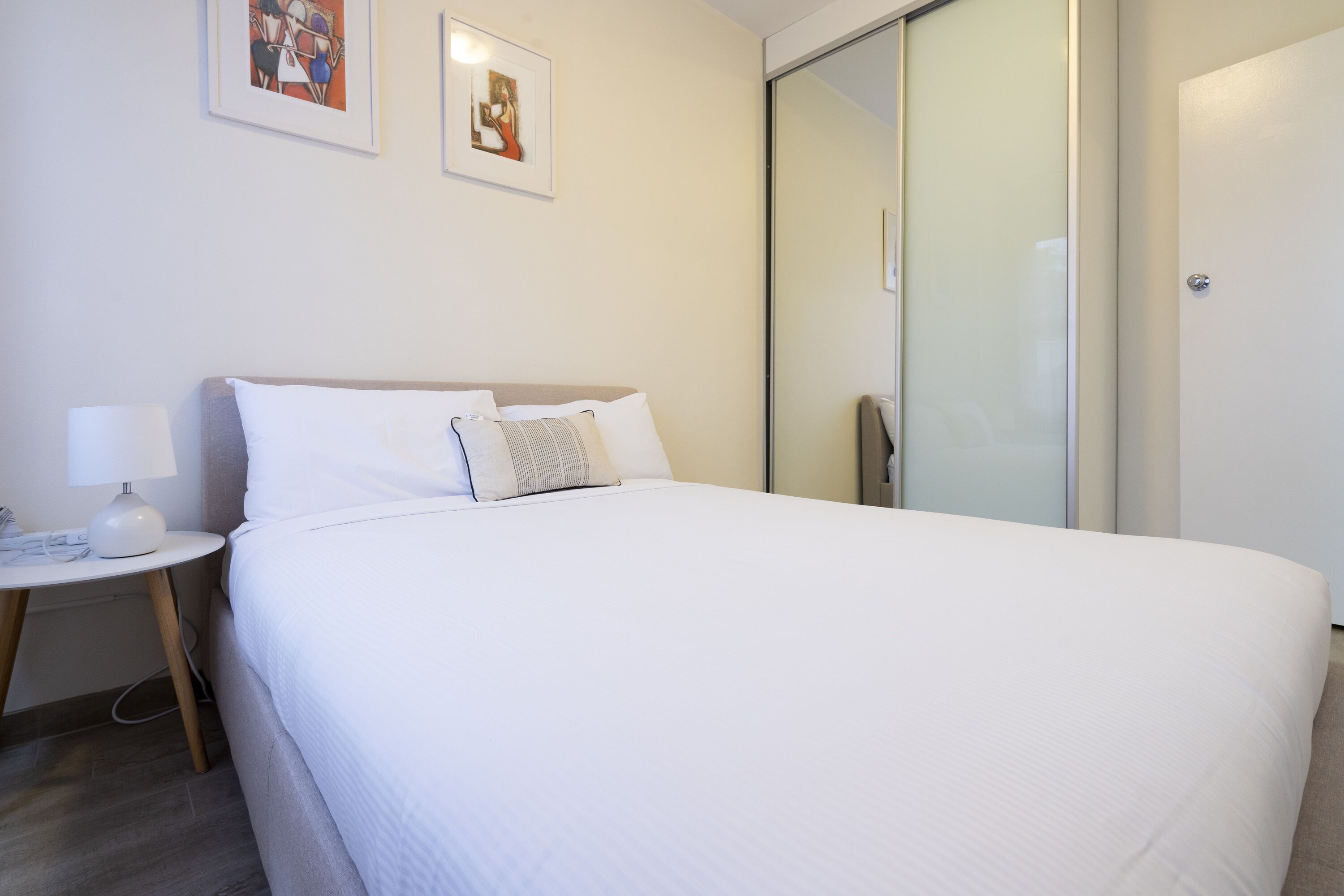 A hotel room with a large bed, a bedside table with a lamp, and a sliding glass door to the bathroom.