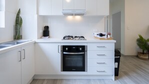 A modern kitchen with white cabinetry, a built-in oven, and a gas stove. - Lotus Stay Manly Apartment 29B (Manly)