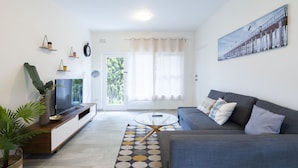 A modern living room with a sofa, TV, and decorative plants. - Lotus Stay Manly Apartment 29B (Manly)