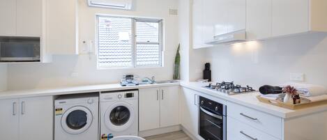 A modern kitchen with white cabinetry, a built-in microwave, a washing machine, and a stove.