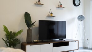 A modern living room with a flat-screen TV on a wooden TV stand, surrounded by plants and minimalist decor. - Lotus Stay Manly Apartment 29B (Manly)