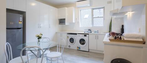 A modern kitchen with a refrigerator, washing machine, and a dining area with a glass table and chairs.