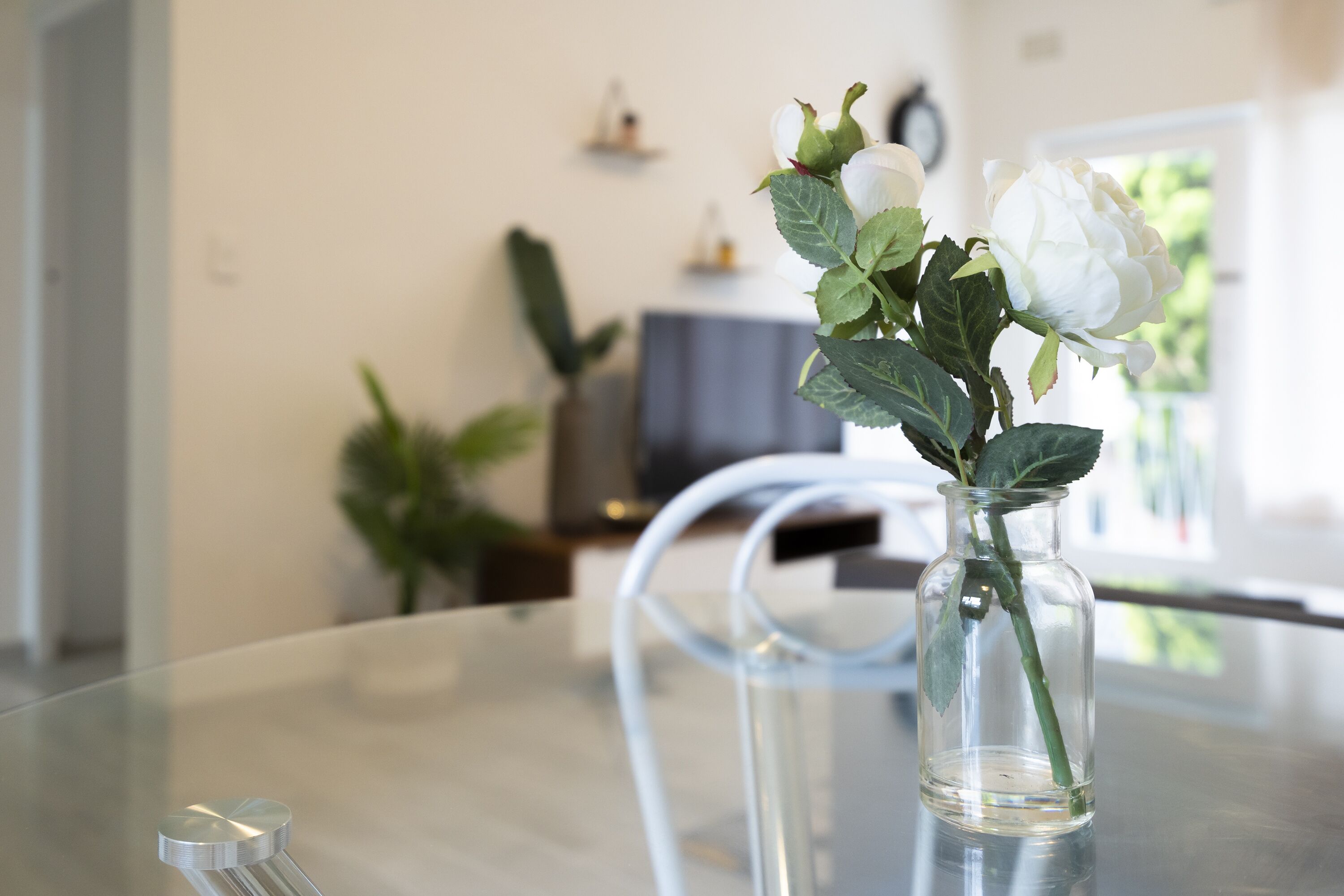 Een glazen vaas met een witte roos op een glazen tafel in een modern interieur.
