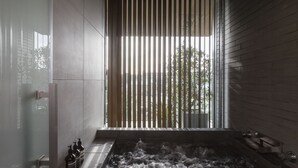 A modern bathroom with a bathtub, a window with vertical blinds, and a shower area. - Hotel Canata Kyoto (Kyoto)