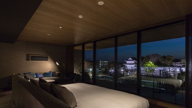 A modern bedroom with a large bed, a seating area, and a view of a cityscape at dusk. - Hotel Canata Kyoto (Kyoto)