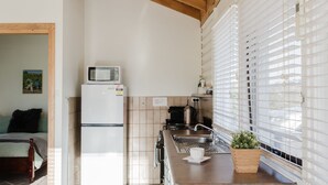 Una cocina compacta con techo de madera, un refrigerador, un microondas, un lavamanos y una ventana con persianas.