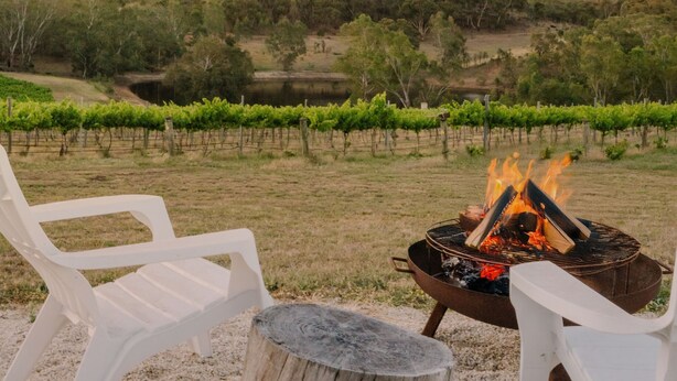 Feuerstelle mit zwei weißen Plastikstühlen und einem hölzernen Baumstumpf inmitten von Weinbergen.