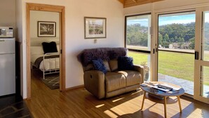 Ein gemütliches Wohnzimmer mit Ledersofa, Couchtisch und Blick auf eine grüne Landschaft durch große Glasüren.