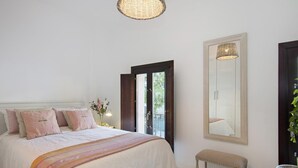 Un dormitorio con una cama grande, un banco, un espejo y una cesta de mimbre.
