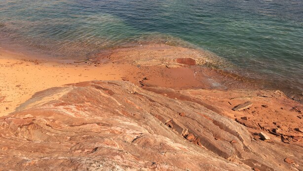 A rocky shoreline with clear water and a sandy beach.