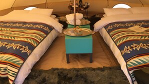 A tented accommodation with two beds, a central table with amenities, and a fur rug on the floor.