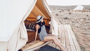 A tent with a person sitting inside, a wooden deck, and another tent in the background.