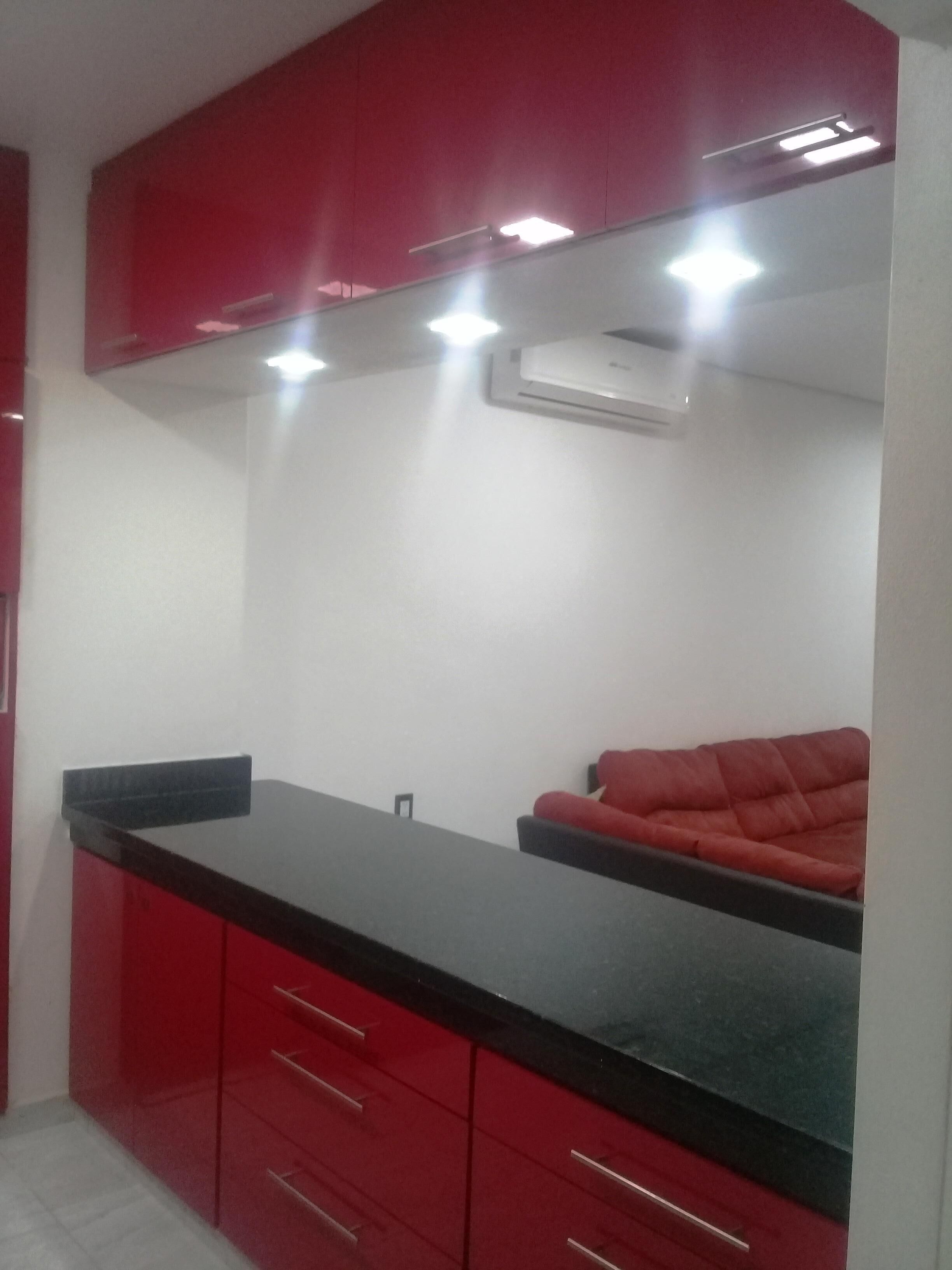 A kitchen with red cabinets, a black countertop, and a red sofa.