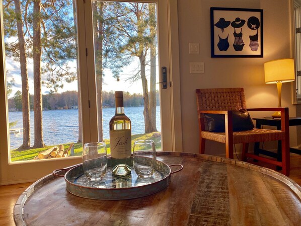 A dining area with a view of a lake, a bottle of wine, and a chair with a cushion.