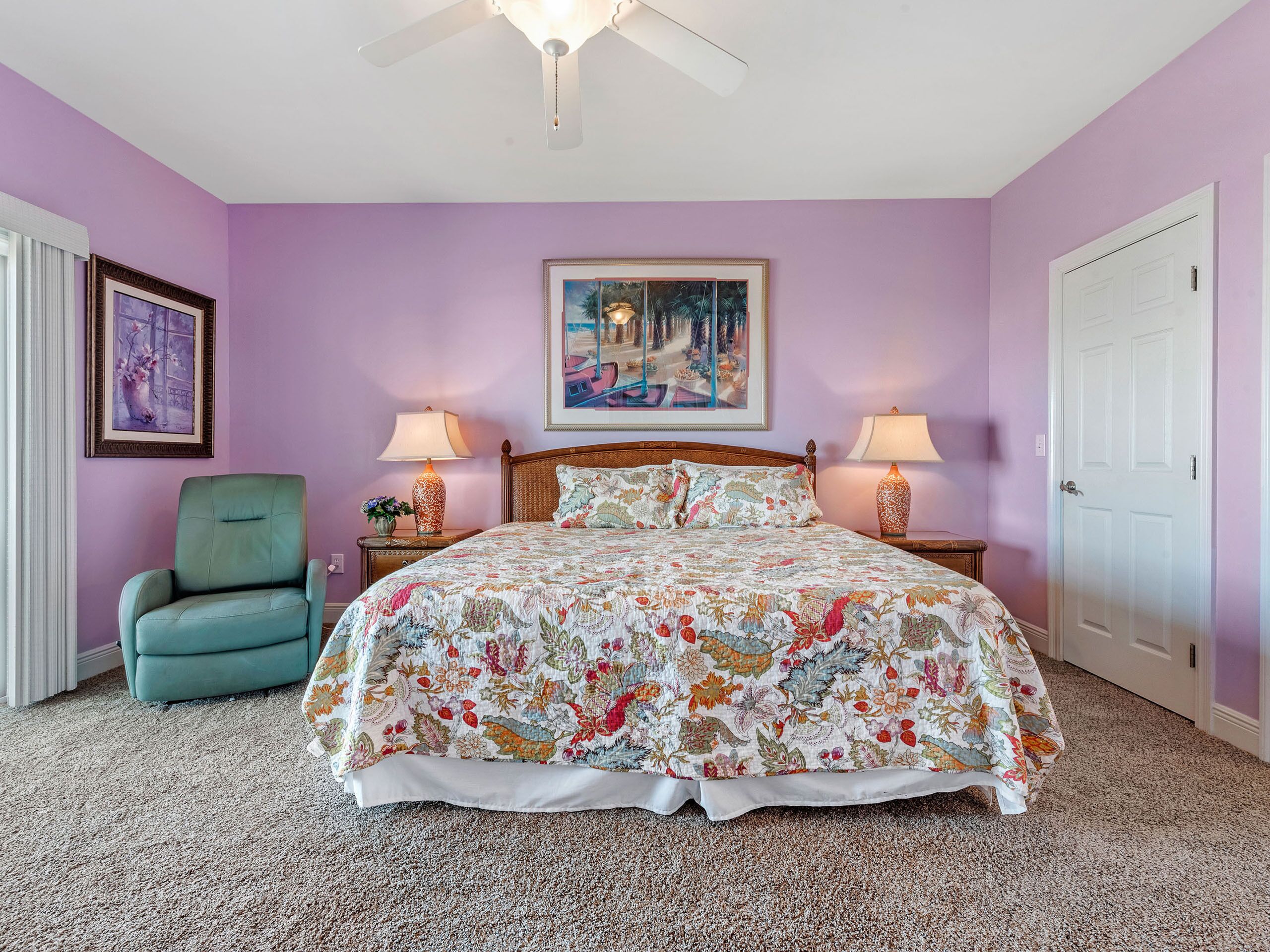 A bedroom with a floral bedspread, a green armchair, two bedside lamps, and a ceiling fan.