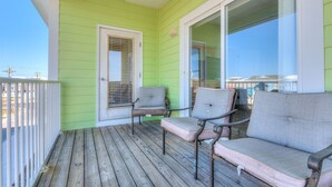 A green porch with two chairs and a table, a sliding glass door, and a view of the ocean. - Sea Urchins, Unit 2. 5 BR. Beachview. The Beach, so close, for less! Pool. (Gulf Shores)