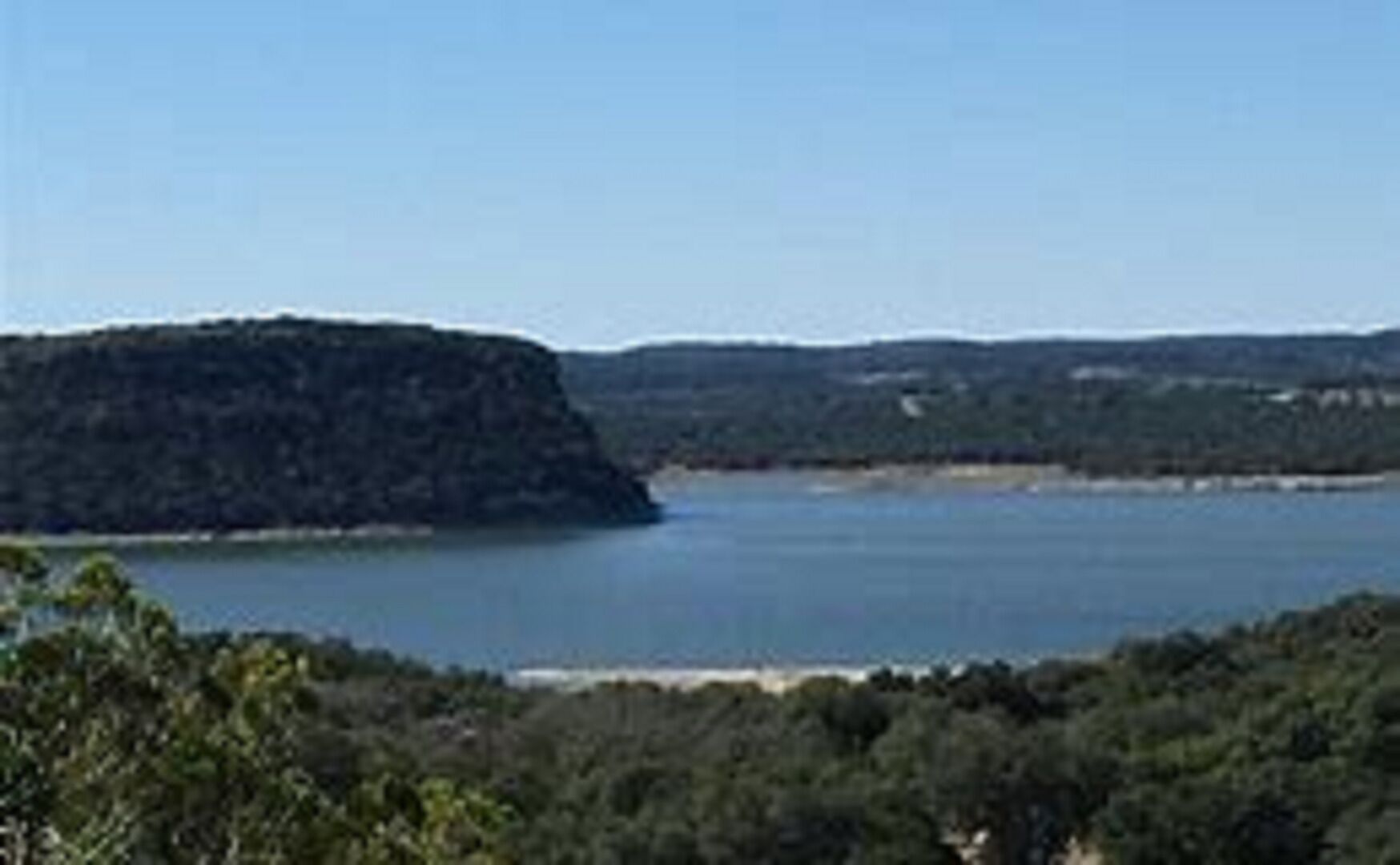Eine Küstenlandschaft mit einem großen Gewässer, einem markanten Hügel und dichter Vegetation.