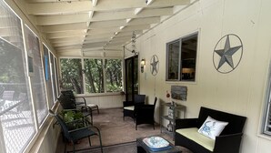 Un'area salotto esterna coperta, con soffitto, divano, poltrona, tavolino e tappeto.