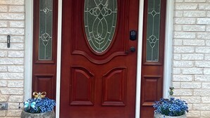 Una porta rossa con un vetrino laterale, affiancata da due vasi con fiori blu, e un muro in pietra.