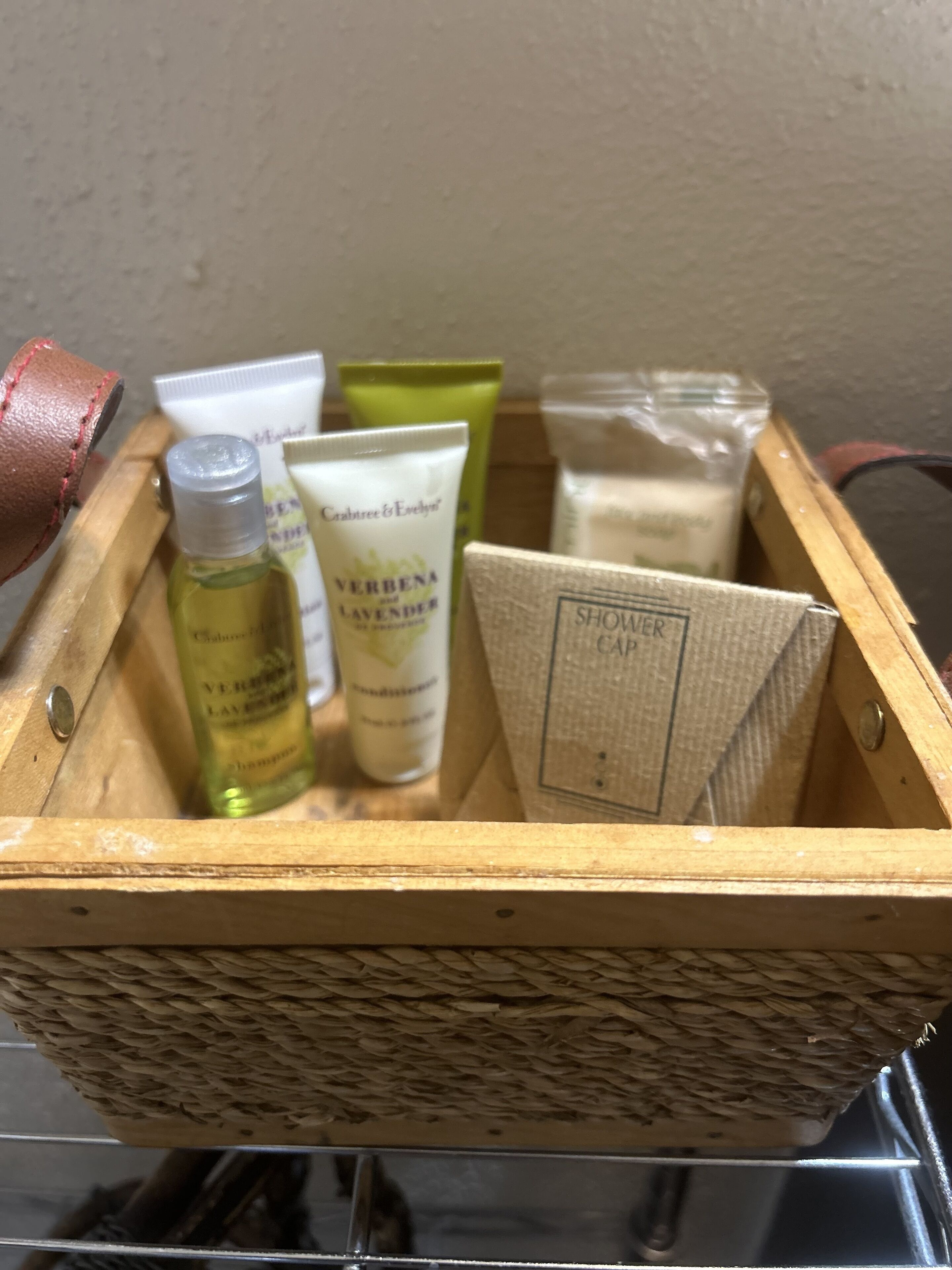 Una caja de madera con varios artículos de aseo personal, incluyendo una botella de champú, un tubo de crema corporal y un gorro de ducha.