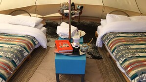 Une pièce confortable aménagée comme une tente, avec deux lits, une petite table sur laquelle se trouve un livre, une bouteille d’eau et une tasse.
