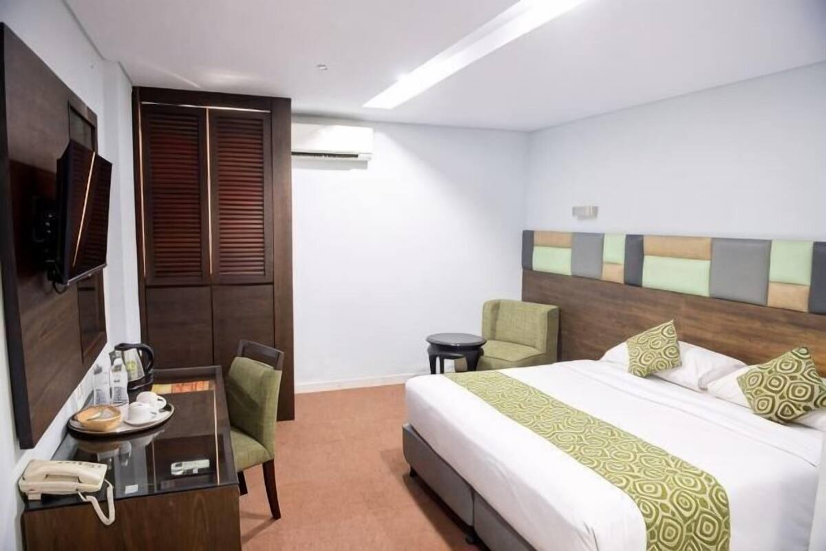 Une chambre d’hôtel comprenant un lit, un bureau avec un téléphone, une chaise, une petite table et un téléviseur fixé au mur.