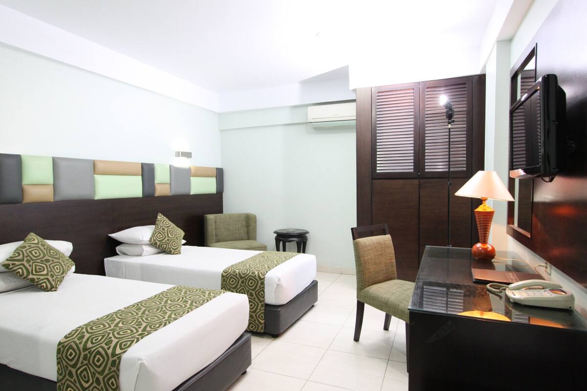 Une chambre d’hôtel avec deux lits, un bureau, une chaise, une lampe, un téléphone et une télévision.