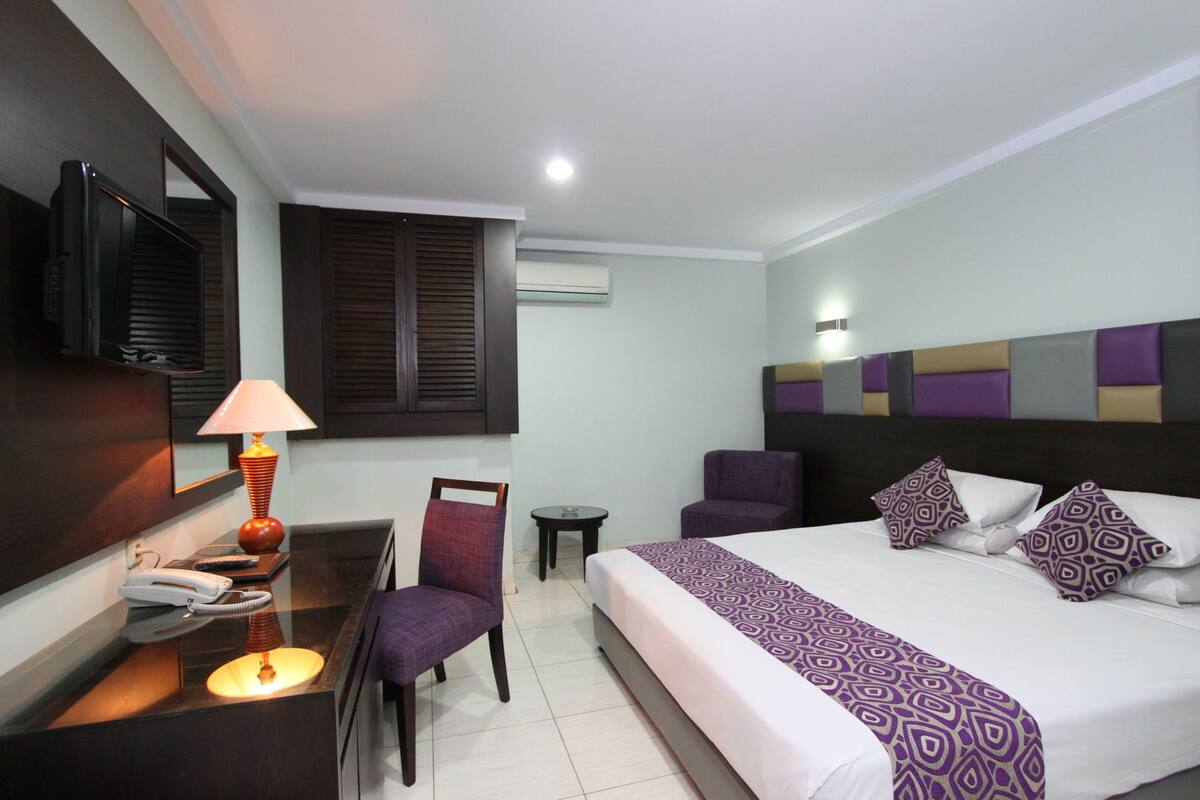 Une chambre d’hôtel comprenant un lit, un bureau avec une lampe, une chaise, une petite table et un téléviseur.