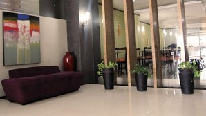A lobby with a red sofa, a large abstract painting, and potted plants. - Hotel Alma (Jakarta)