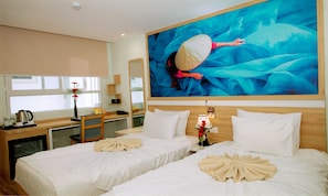 Two beds with white linens and decorative pillows, a large painting, and a wooden desk with a coffee maker and vase.